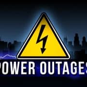 Warning sign for power outage against a dark city skyline.